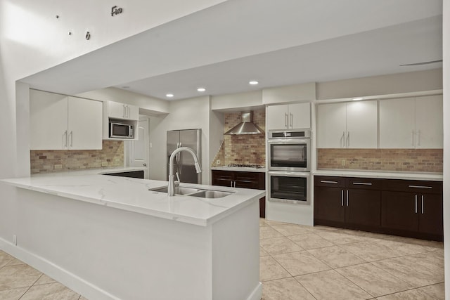 kitchen with appliances with stainless steel finishes, sink, dark brown cabinetry, kitchen peninsula, and wall chimney range hood