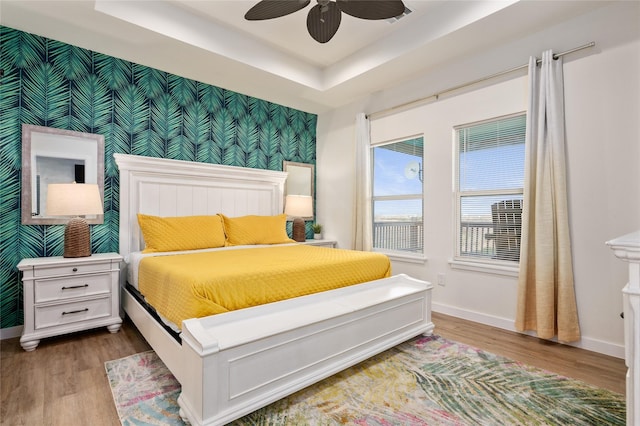 bedroom with ceiling fan, a raised ceiling, and hardwood / wood-style floors