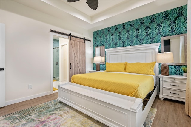 bedroom featuring hardwood / wood-style flooring, a barn door, a raised ceiling, and ensuite bathroom