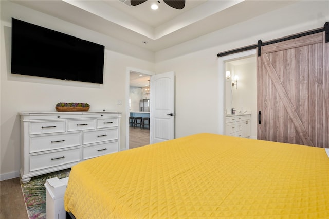 bedroom with ceiling fan, hardwood / wood-style flooring, connected bathroom, and a barn door