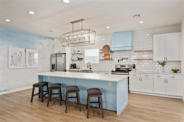 kitchen featuring appliances with stainless steel finishes, a kitchen bar, a center island, premium range hood, and white cabinets