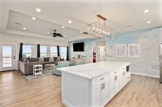 kitchen with white cabinetry, light stone counters, hanging light fixtures, a kitchen island, and light hardwood / wood-style floors