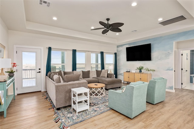 living room with light wood-type flooring, a tray ceiling, and ceiling fan