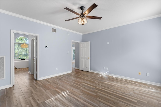 empty room with ornamental molding, wood finished floors, visible vents, and baseboards