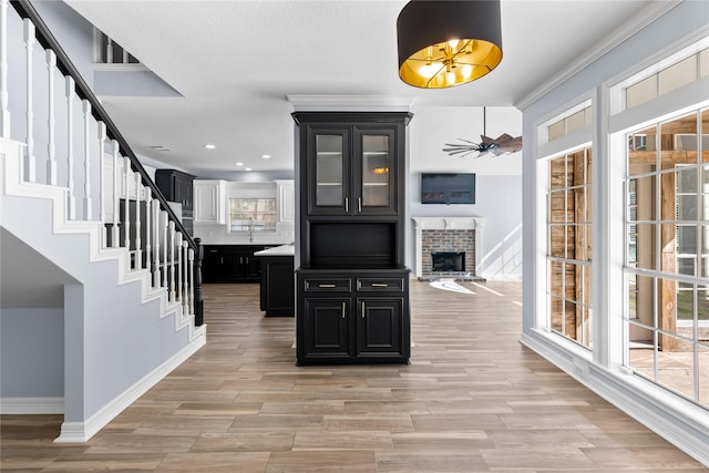 interior space with light wood-type flooring, a brick fireplace, stairs, and baseboards