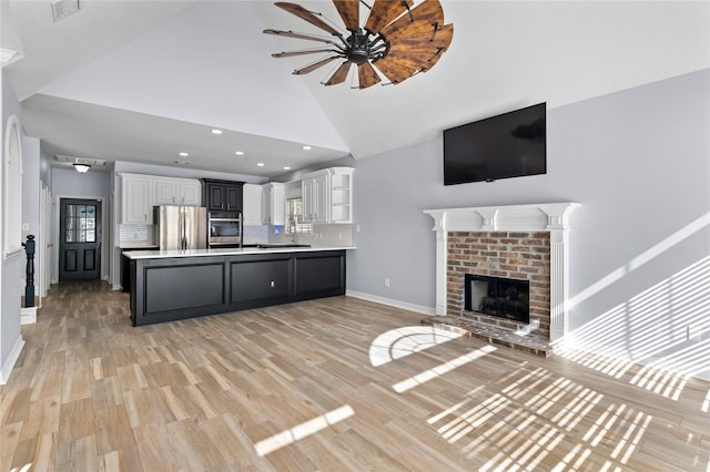 unfurnished living room with high vaulted ceiling, a fireplace, a sink, baseboards, and light wood finished floors