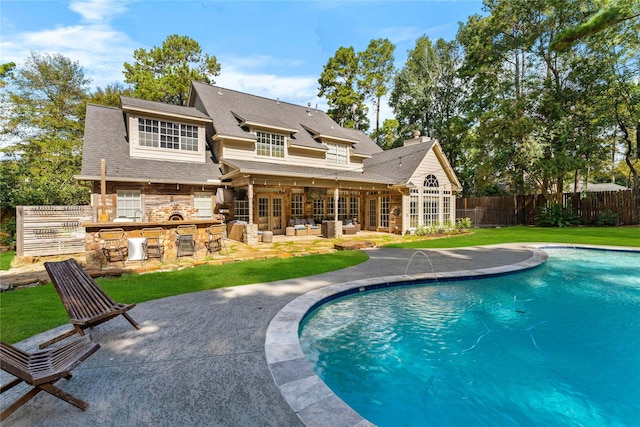 back of property featuring fence, outdoor dry bar, a lawn, a fenced in pool, and a patio area