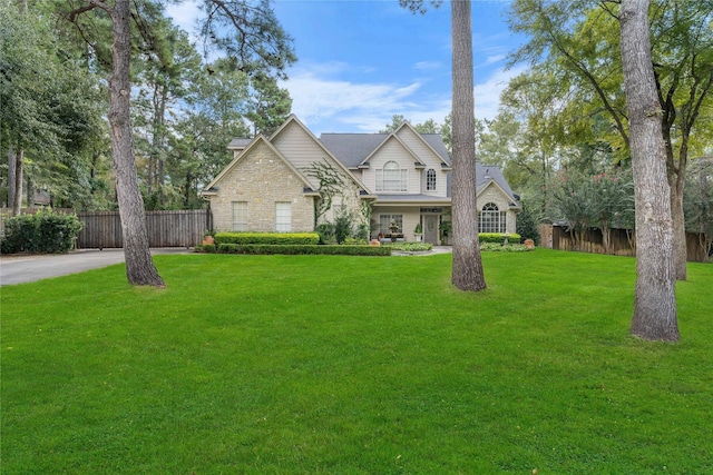 view of front of home with a front yard, stone siding, and fence