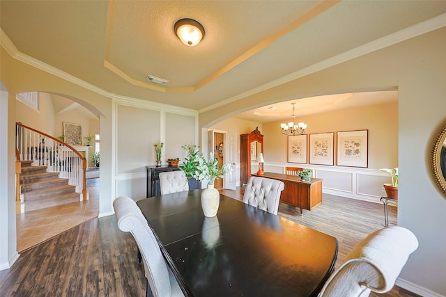 dining area featuring crown molding, a tray ceiling, wood-type flooring, and a chandelier