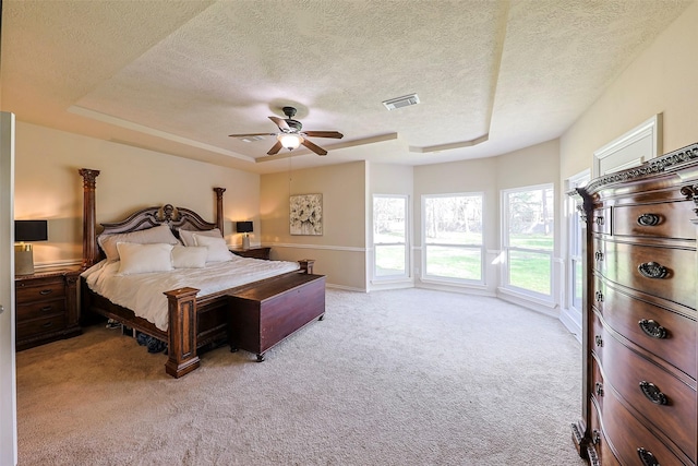 bedroom featuring ceiling fan, a tray ceiling, light carpet, and a textured ceiling