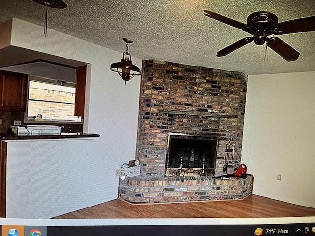 unfurnished living room with a brick fireplace, hardwood / wood-style flooring, a textured ceiling, and ceiling fan