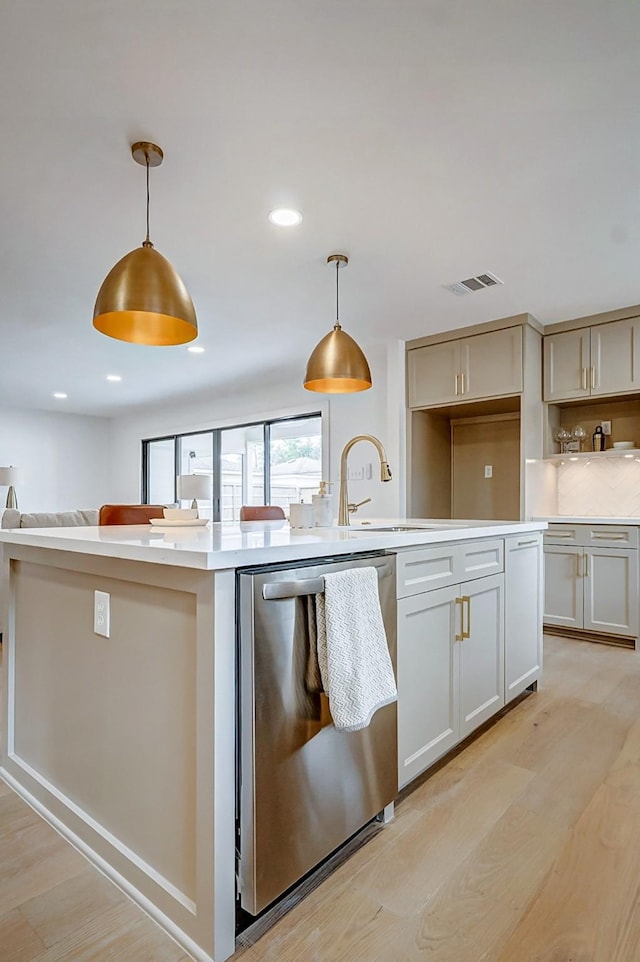 kitchen with sink, light hardwood / wood-style flooring, a kitchen island with sink, hanging light fixtures, and stainless steel dishwasher