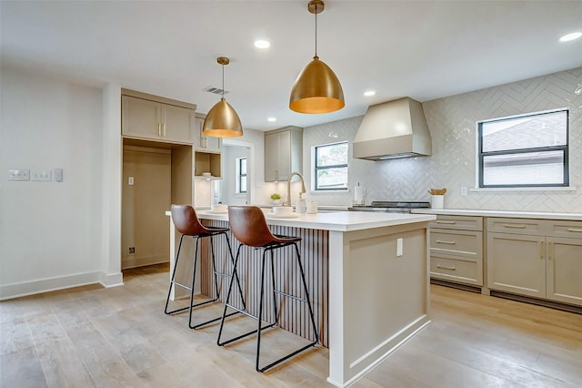 kitchen featuring premium range hood, a kitchen island with sink, light hardwood / wood-style floors, and decorative light fixtures