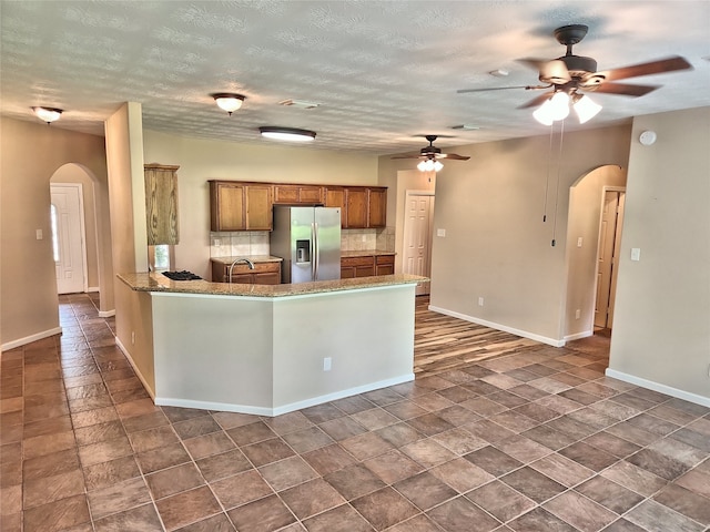 kitchen with stainless steel fridge, ceiling fan, backsplash, a textured ceiling, and kitchen peninsula