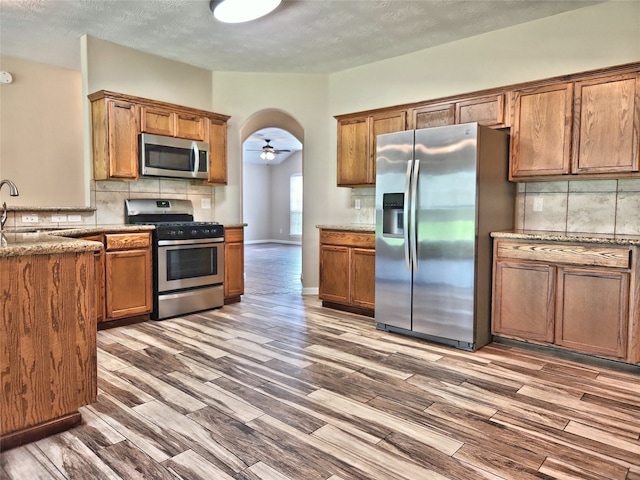 kitchen featuring ceiling fan, stainless steel appliances, wood-type flooring, and decorative backsplash