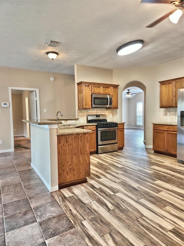 kitchen with sink, dark hardwood / wood-style flooring, light stone counters, ceiling fan, and stainless steel appliances