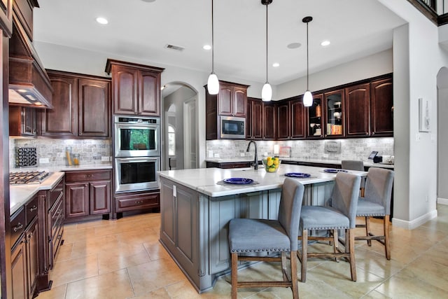 kitchen with dark brown cabinetry, appliances with stainless steel finishes, a kitchen breakfast bar, and an island with sink