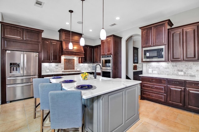 kitchen with appliances with stainless steel finishes, decorative light fixtures, a kitchen breakfast bar, light stone counters, and a center island with sink