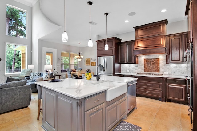 kitchen with decorative light fixtures, an island with sink, dark brown cabinetry, light stone counters, and stainless steel appliances