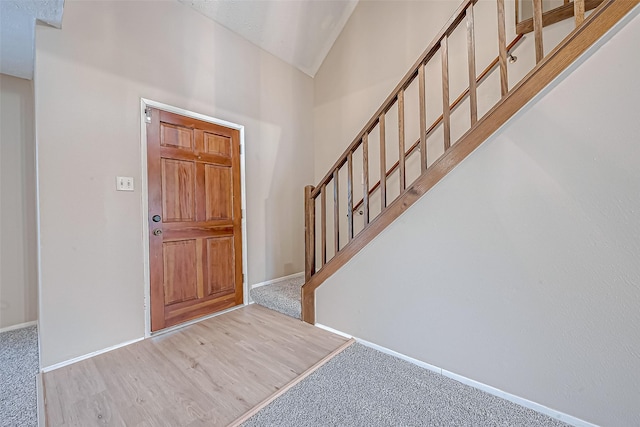 carpeted entrance foyer featuring stairway, baseboards, lofted ceiling, and wood finished floors