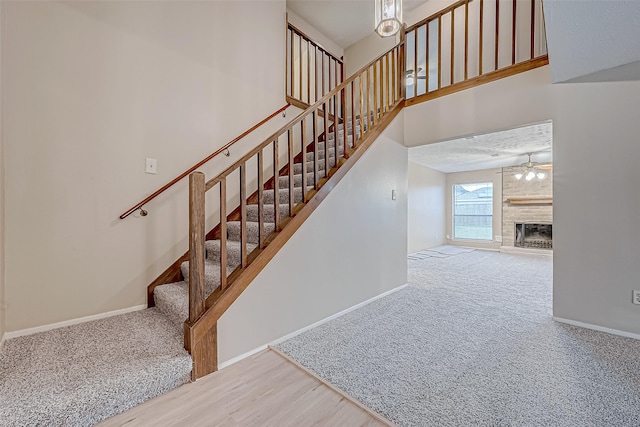 staircase featuring a high ceiling, ceiling fan, carpet flooring, and a fireplace