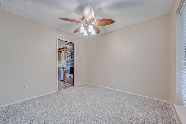 spare room featuring light colored carpet, a textured ceiling, baseboards, and ceiling fan