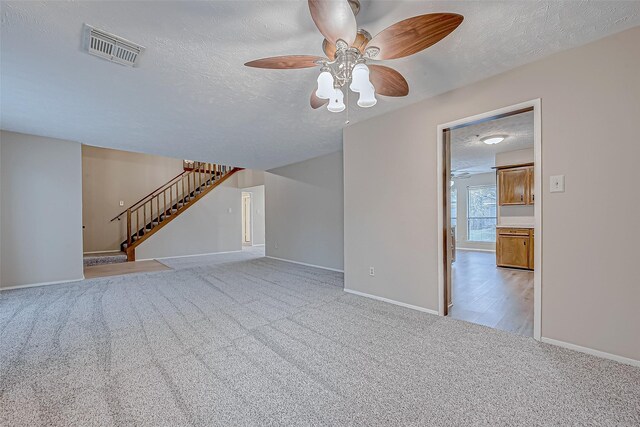 unfurnished living room featuring ceiling fan, light colored carpet, and a textured ceiling