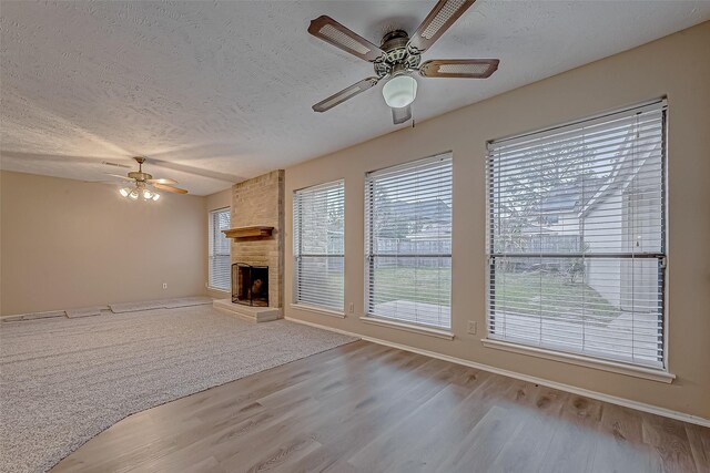 unfurnished living room with ceiling fan, a fireplace, light hardwood / wood-style floors, and a textured ceiling