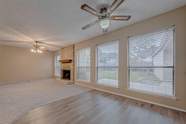 unfurnished living room with a textured ceiling, a large fireplace, a ceiling fan, and wood finished floors