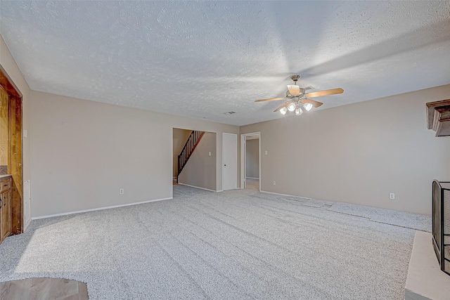 unfurnished living room featuring light colored carpet, ceiling fan, stairs, and a textured ceiling