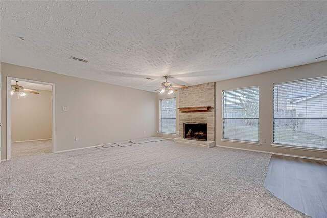 unfurnished living room with carpet, visible vents, ceiling fan, a textured ceiling, and a brick fireplace