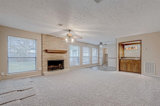 unfurnished living room with ceiling fan, light colored carpet, a fireplace, and a textured ceiling