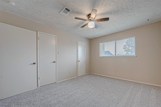 unfurnished bedroom featuring carpet flooring, a ceiling fan, visible vents, and a textured ceiling