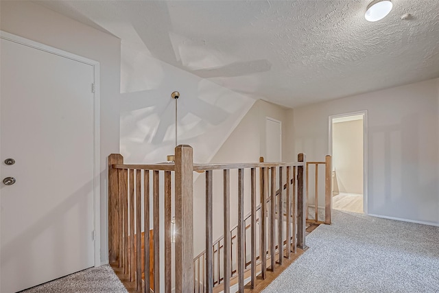 hall featuring an upstairs landing, a textured ceiling, and carpet floors