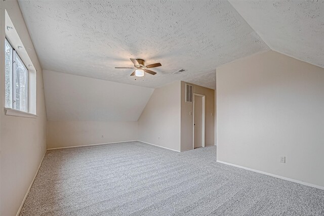 additional living space featuring vaulted ceiling, carpet, ceiling fan, and a textured ceiling