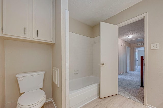 bathroom with hardwood / wood-style floors, a textured ceiling, shower / washtub combination, and toilet