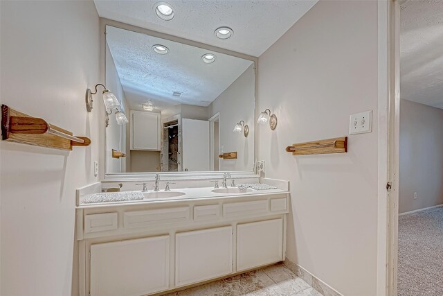 full bath with a sink, baseboards, a textured ceiling, and double vanity