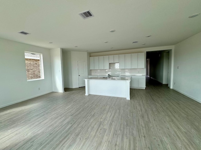 kitchen featuring white cabinetry, an island with sink, sink, decorative backsplash, and light wood-type flooring