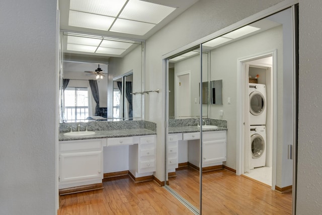 laundry room with sink, light hardwood / wood-style flooring, stacked washer and clothes dryer, and ceiling fan