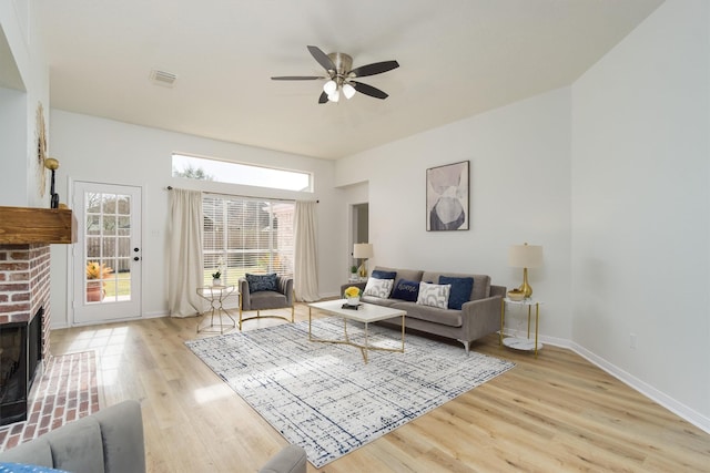 living room with a fireplace, ceiling fan, and light wood-type flooring