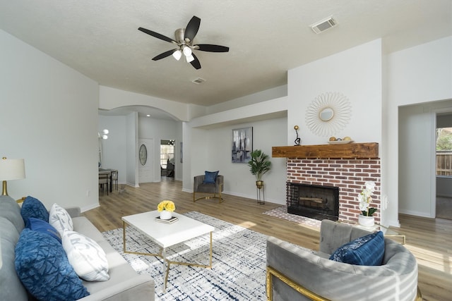 living room featuring ceiling fan, a fireplace, light hardwood / wood-style flooring, and a textured ceiling