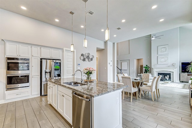 kitchen with white cabinetry, sink, light stone counters, stainless steel appliances, and a center island with sink