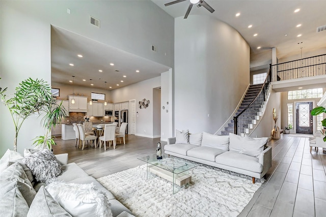 living room featuring a towering ceiling, light hardwood / wood-style floors, and ceiling fan