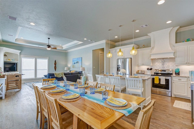 dining room featuring ceiling fan, ornamental molding, a raised ceiling, and light hardwood / wood-style flooring