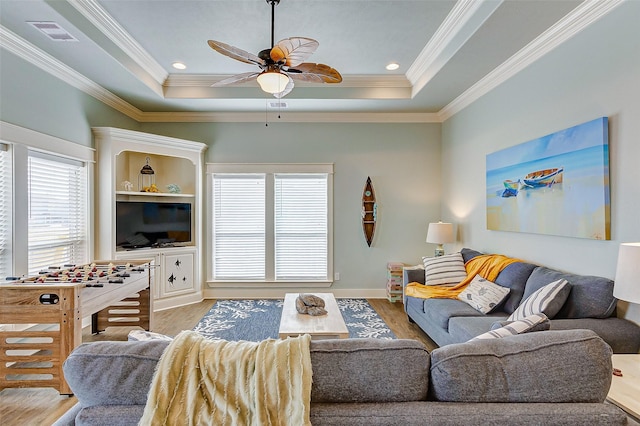 living room featuring a raised ceiling, wood-type flooring, and crown molding