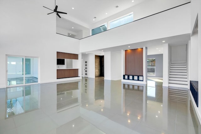 interior space with a towering ceiling, light tile patterned floors, and ceiling fan