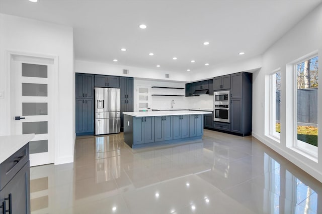 kitchen with sink, a kitchen island, light tile patterned flooring, and appliances with stainless steel finishes