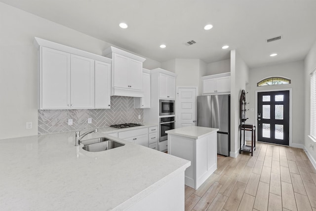 kitchen featuring sink, a center island, appliances with stainless steel finishes, white cabinets, and backsplash