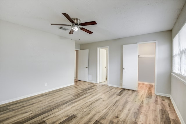 unfurnished bedroom featuring connected bathroom, a walk in closet, ceiling fan, light wood-type flooring, and a closet