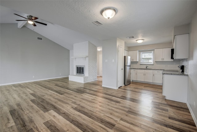 kitchen featuring sink, stainless steel refrigerator, light stone counters, a fireplace, and white cabinets